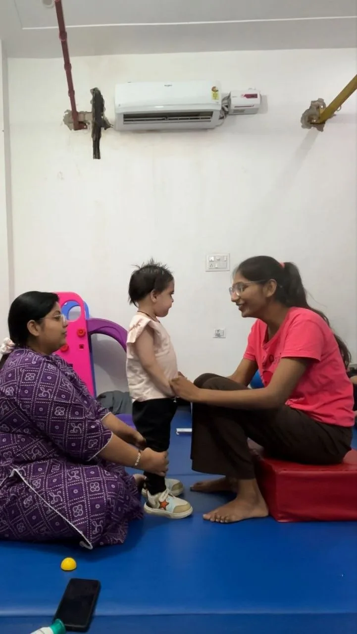Two adults supporting a child during a standing activity